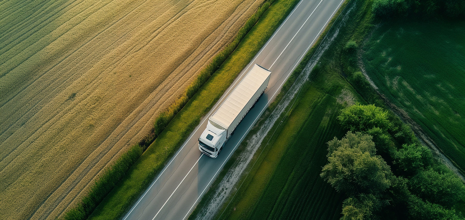 Ariel view of a lorry careening down a road with with a meadow and bunch of trees either side